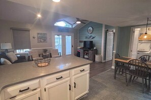 A kitchen with a central island, a dining area with a table and chairs, a ceiling fan, and a clock on the wall. - 1495 Ocean Lakes Golf Cart ⛱️🏝️🩱🌊👙☀️🐚 (Myrtle Beach)
