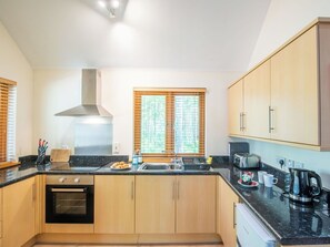 Eine moderne Küche mit Holzschränken, einer schwarzen Arbeitsplatte, einem Herd, einer Spüle und einem Fenster mit Jalousien.