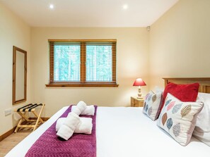 Ein Hotelzimmer mit Bett, Fenster mit Jalousien, Nachttischlampe und einem Holzboden.