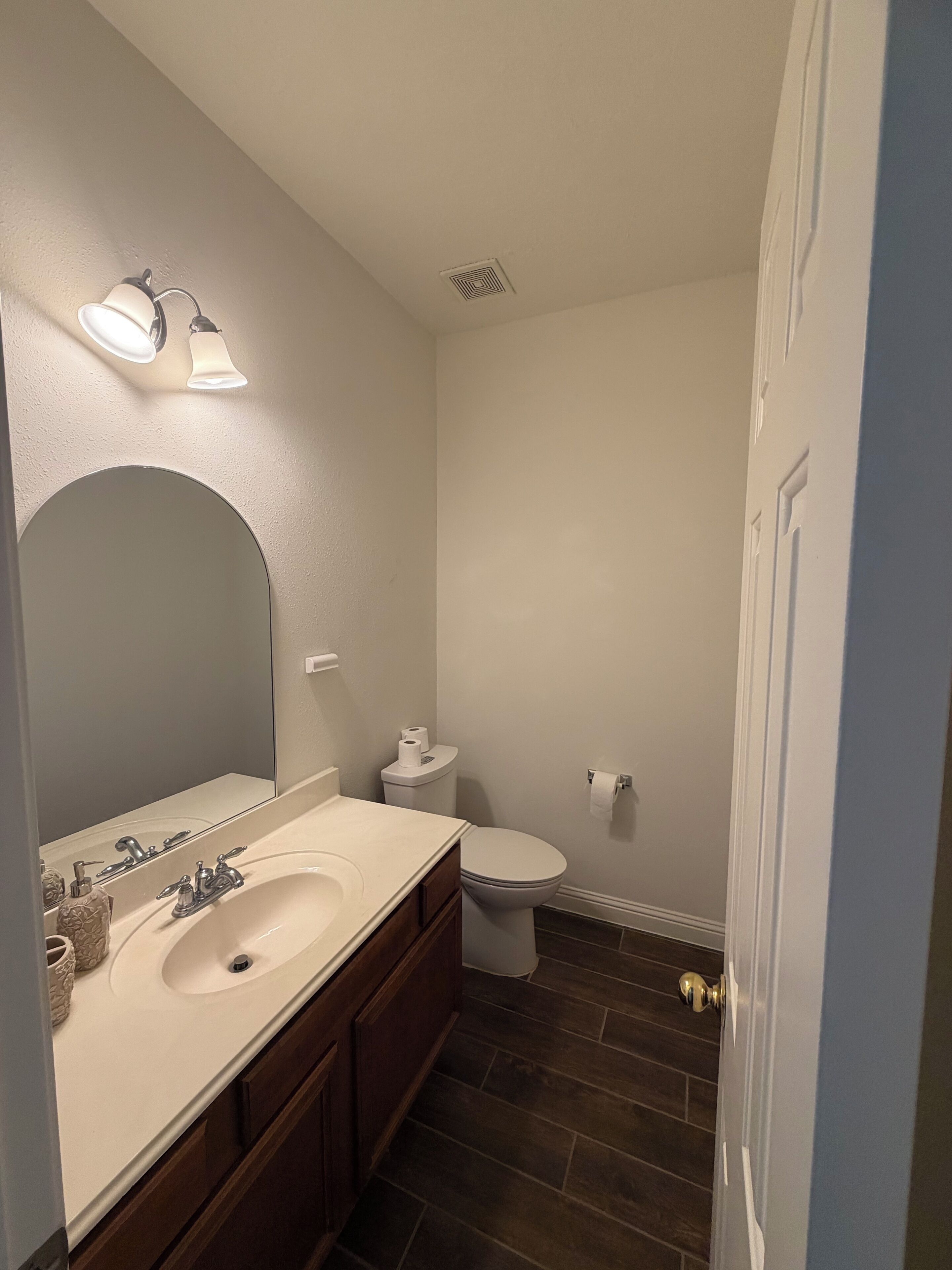 A bathroom with a sink, mirror, toilet, and a door.