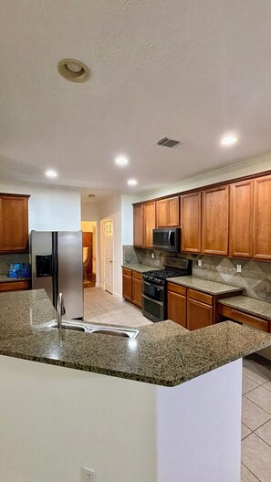 Una cocina moderna con encimeras de granito, electrodomésticos de acero inoxidable y armarios de madera.