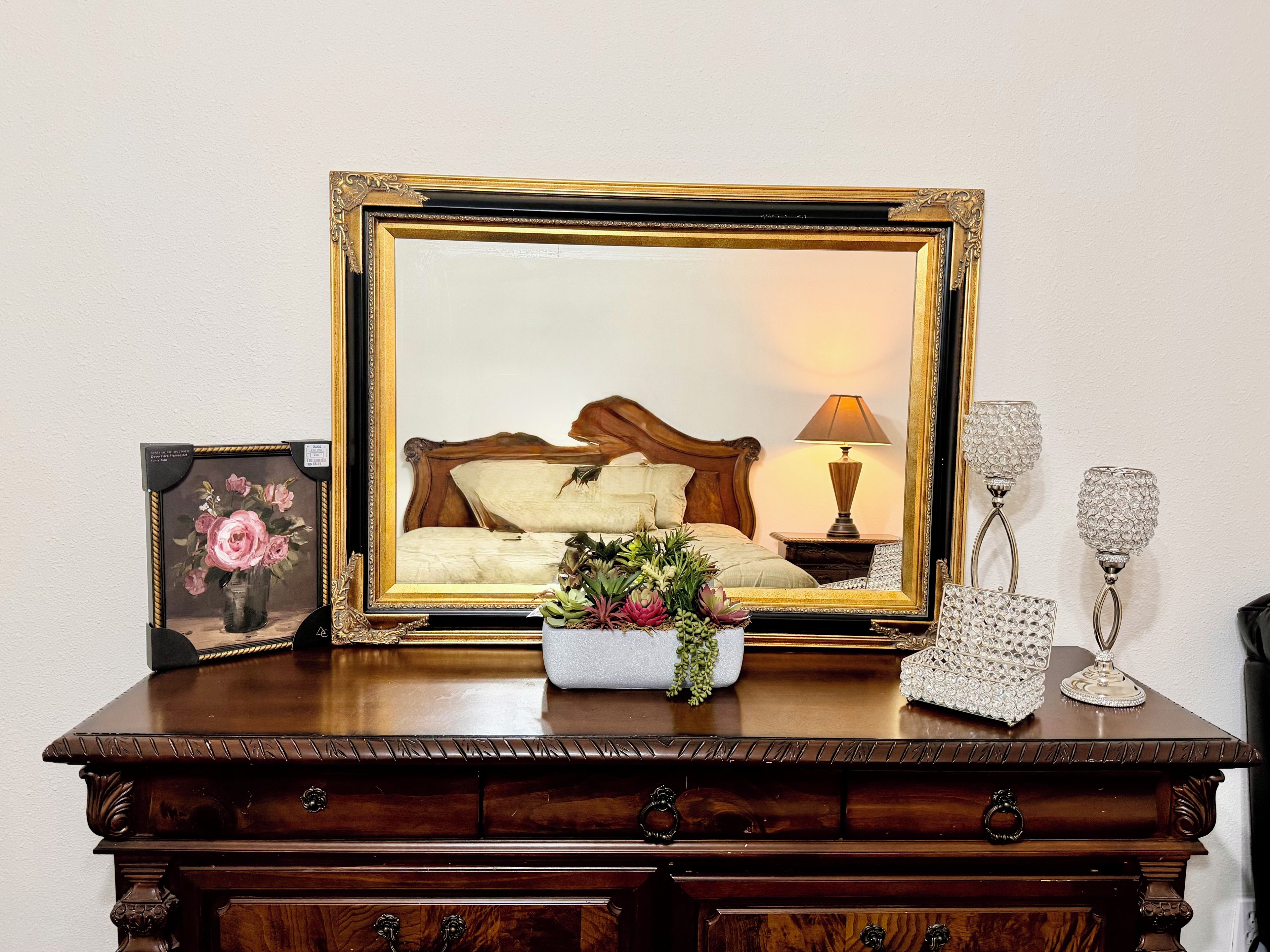 Un aparador de madera con espejo, un cuadro enmarcado, una lámpara y objetos decorativos.