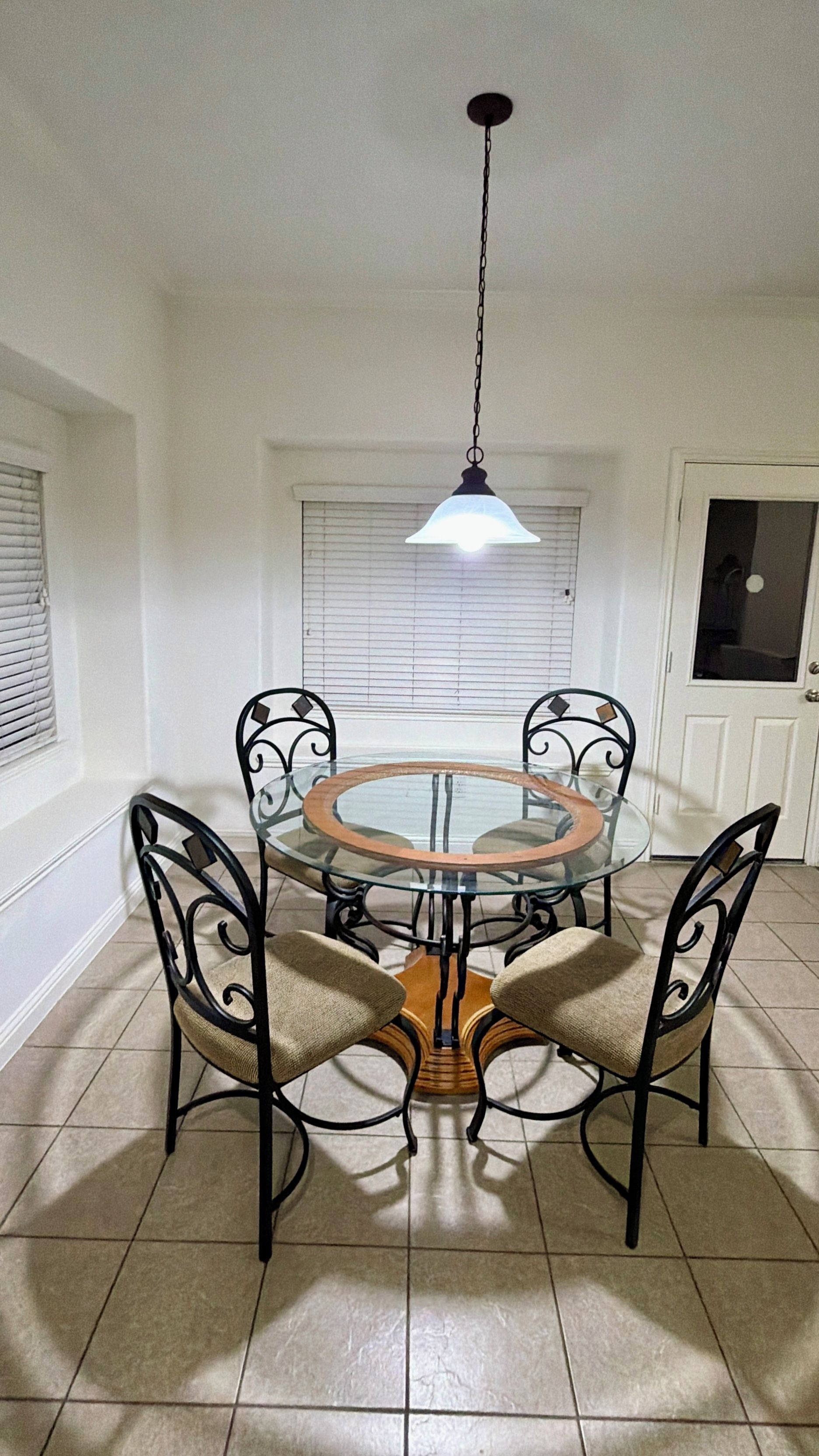 A dining area with a glass table and four chairs, a hanging light fixture, and a door with a window.