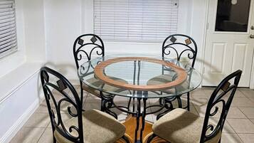 A dining area with a glass table and four chairs, a hanging light fixture, and a door with a window.
