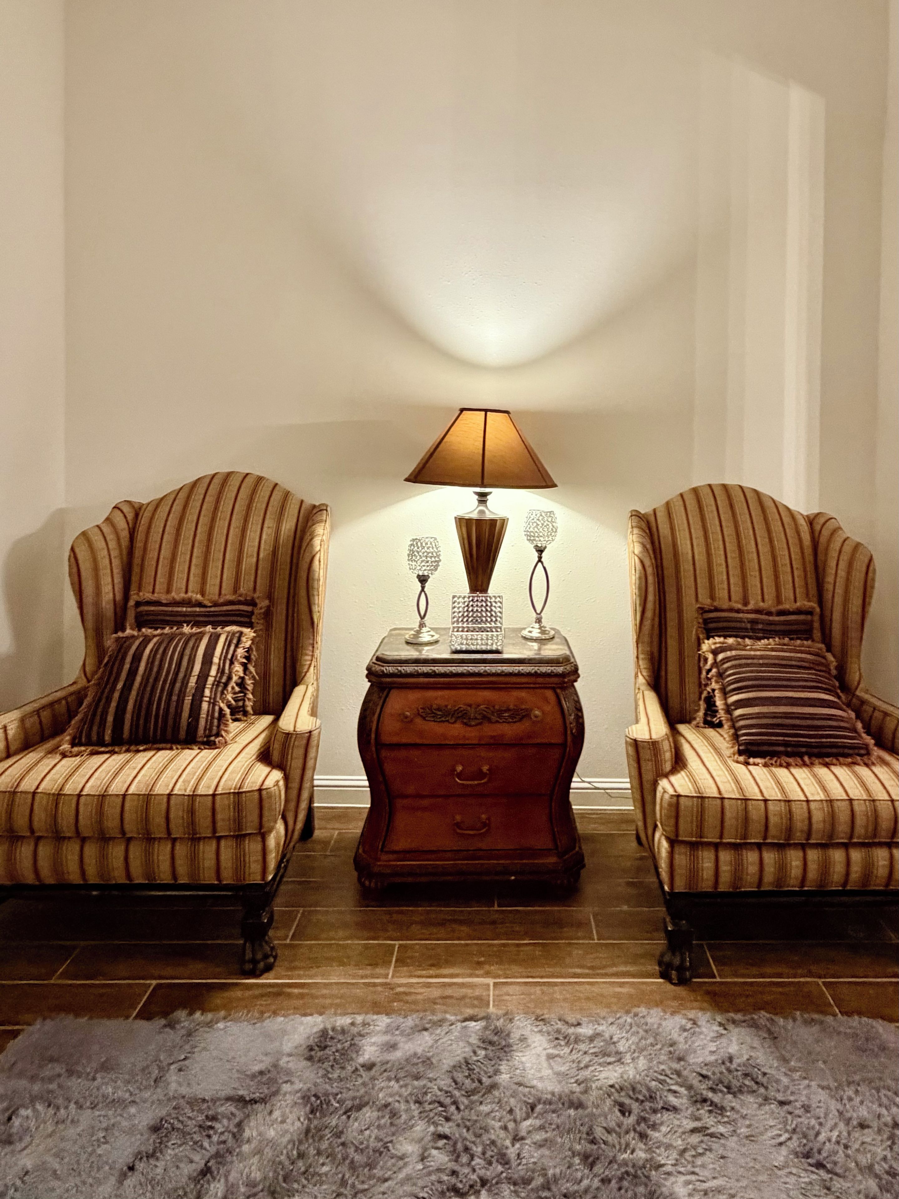 A room with two armchairs, a small wooden side table with a lamp, and a fluffy rug.