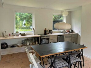 A modern kitchen with a dining area, large windows, and a view of greenery. - Bright 1960s house with natural plot near beach (Højbyb)