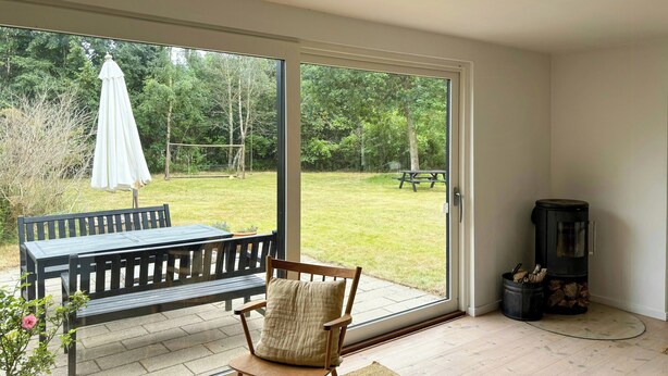 Ein Zimmer mit einer Glastür zum Garten, einer hölzernen Bank, einem Sessel mit Kissen und einem Kamin.