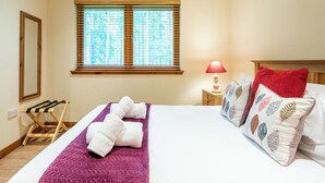 Ein Hotelzimmer mit Bett, Fenster mit Jalousien, Nachttischlampe und einem Holzboden.