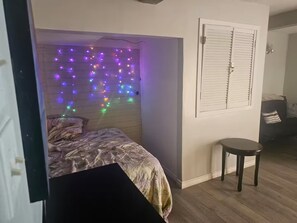 A bedroom with a bed, a small round table, and colorful string lights on the wall.