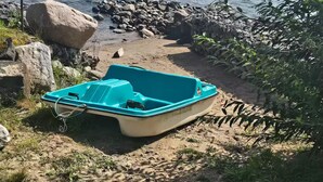 A boat on a sandy shore with a body of water and hills in the background.