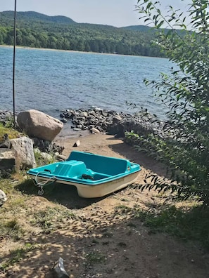 A boat on a sandy shore with a body of water and hills in the background.