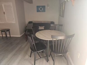 A dining area with a round table and six chairs, a sofa, and a small table with a chair.