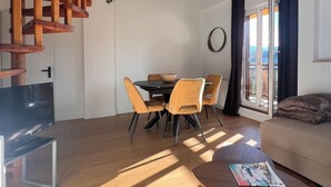 A modern living space with a wooden staircase, a dining area with a table and chairs, a sofa, and a large window with curtains. - Le Chic Panoramique - Mountain and City Views - Villard de Lans (Villard-de-Lans)