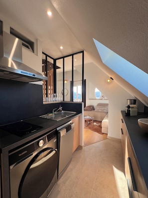 Eine moderne Küche mit Geschirrspüler, Herd und Spüle. Ein Essbereich mit Tisch und Stühlen lädt zum Verweilen ein, und ein Dachfenster bietet einen Blick ins Freie.