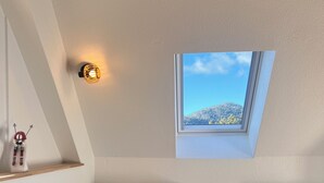 A cozy room with a sloped ceiling, a built-in skylight, a cushioned sectional sofa, and a small shelf with a decorative item. - Le Chic Panoramique - Mountain and City Views - Villard de Lans (Villard-de-Lans)