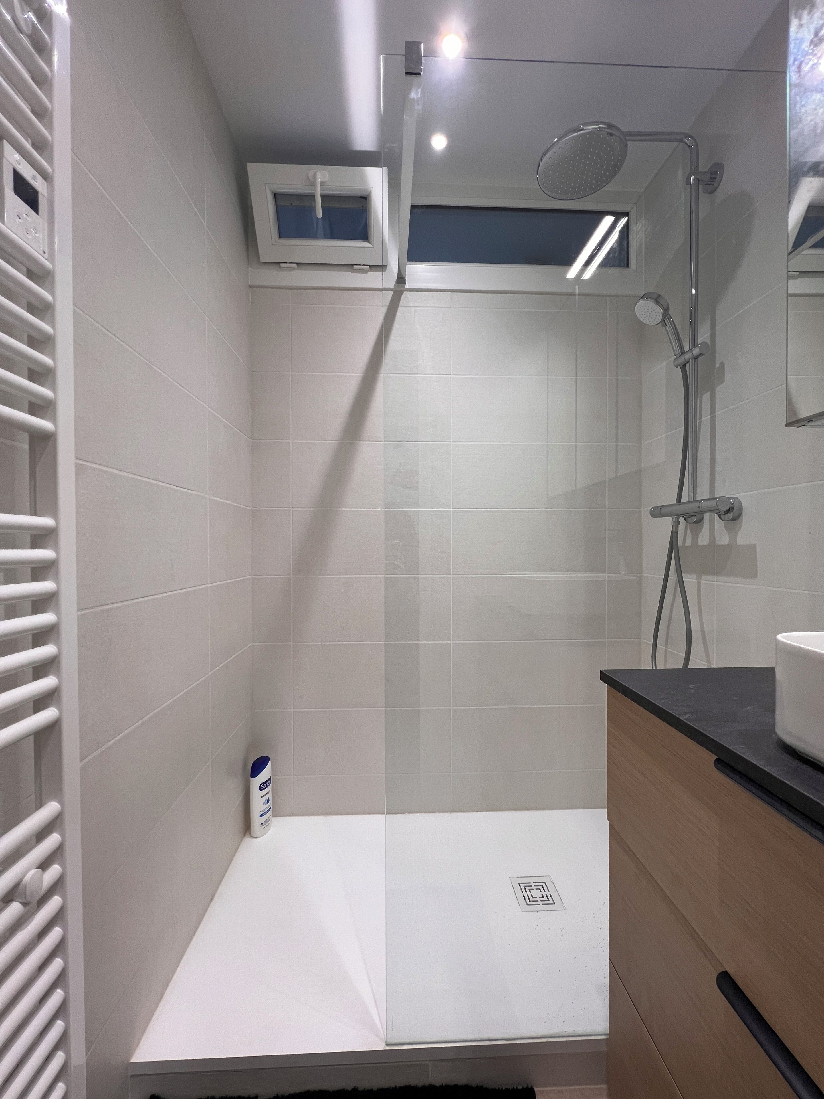 Une salle de bain avec des carreaux blancs, une douche, des toilettes et un lavabo.