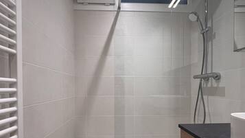 Une salle de bain avec des carreaux blancs, une douche, des toilettes et un lavabo.