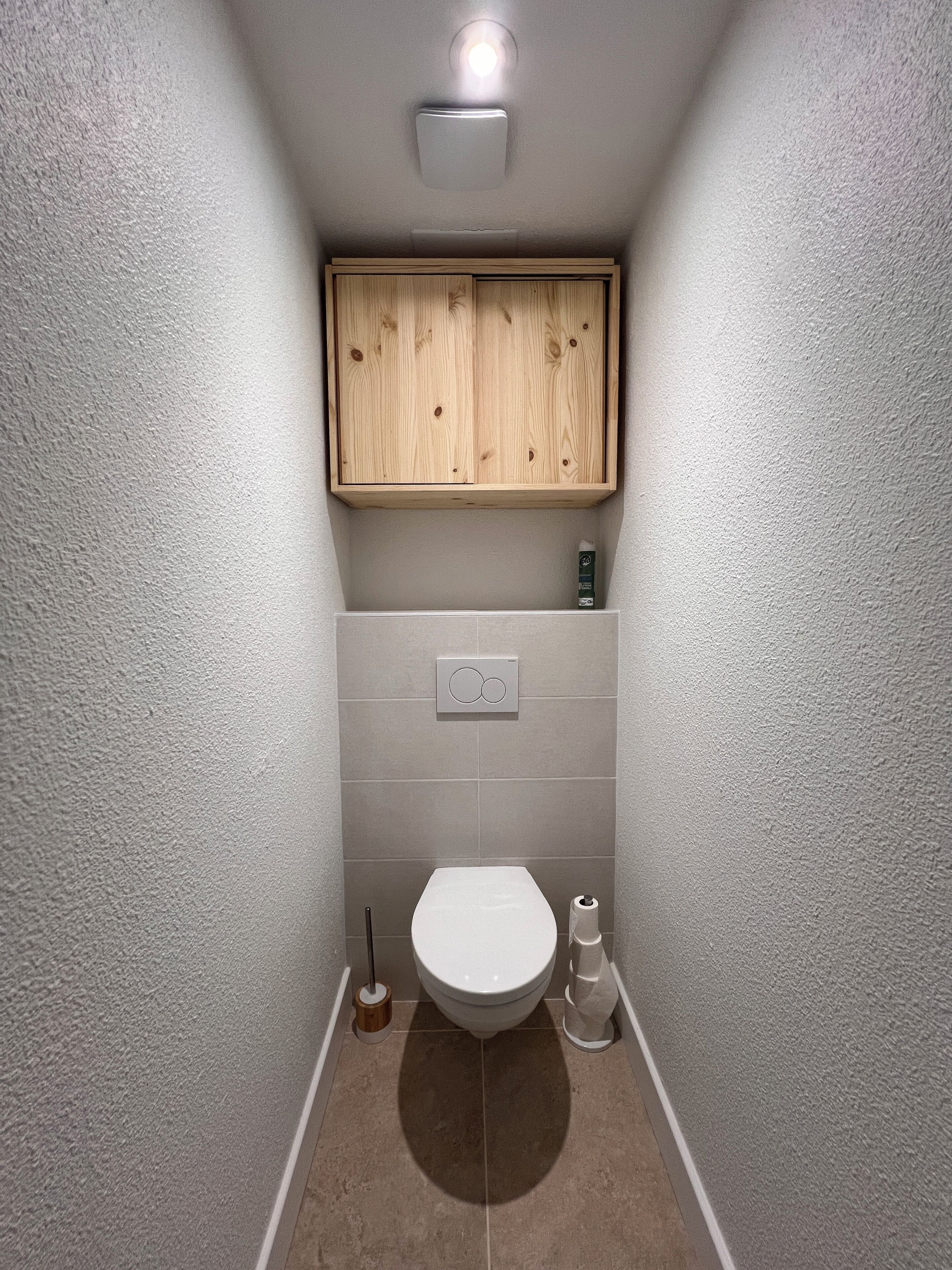 Une petite salle de bain avec des toilettes, un meuble en bois au-dessus du lavabo et un porte-rouleau de papier toilette fixé au mur.