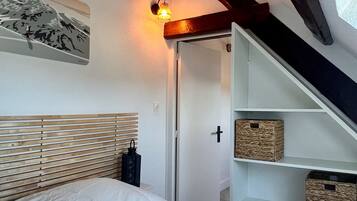 Een slaapkamer met een bed, wandlamp, houten hoofdbord en een ingebouwde wandplank met manden.