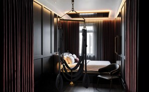 Ein modernes Hotelzimmer mit einem Bett, einem Sessel, einem Hängekorbstuhl und einem Fernseher.