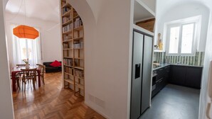 Et moderne køkken med indbygget køleskab, et spiseområde med et træbord og stole, samt en reol fyldt med bøger.