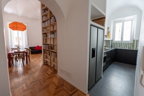 Eine moderne Küche mit einem eingebauten Kühlschrank, eine Essecke mit einem Holztisch und Stühlen sowie ein Bücherregal voller Bücher.