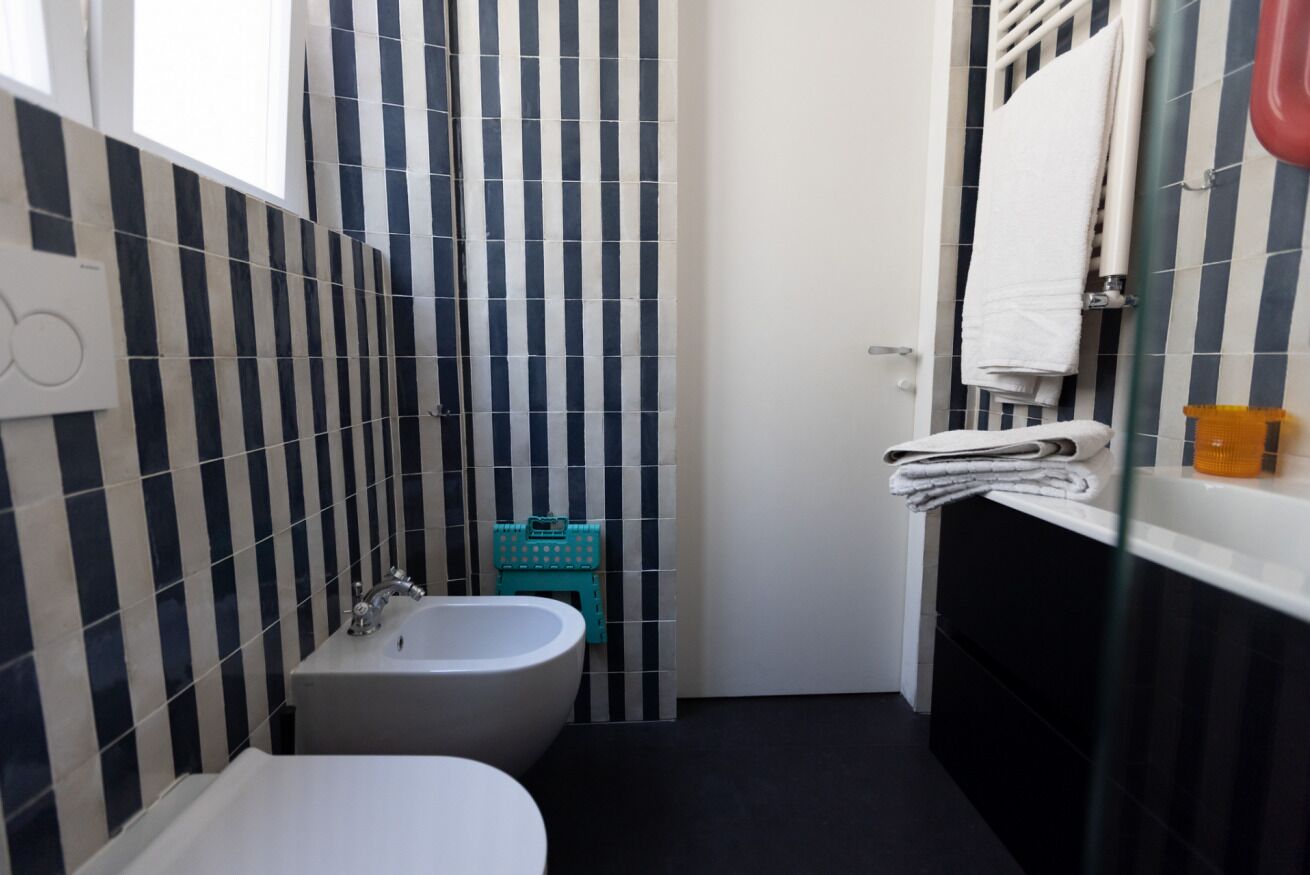 A bathroom with a bathtub, a toilet, and a sink. There is a towel rack with towels and a glass shower door.
