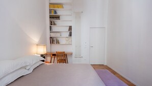 Et soveværelse med seng, skrivebord, stol, bogreol og en dør.