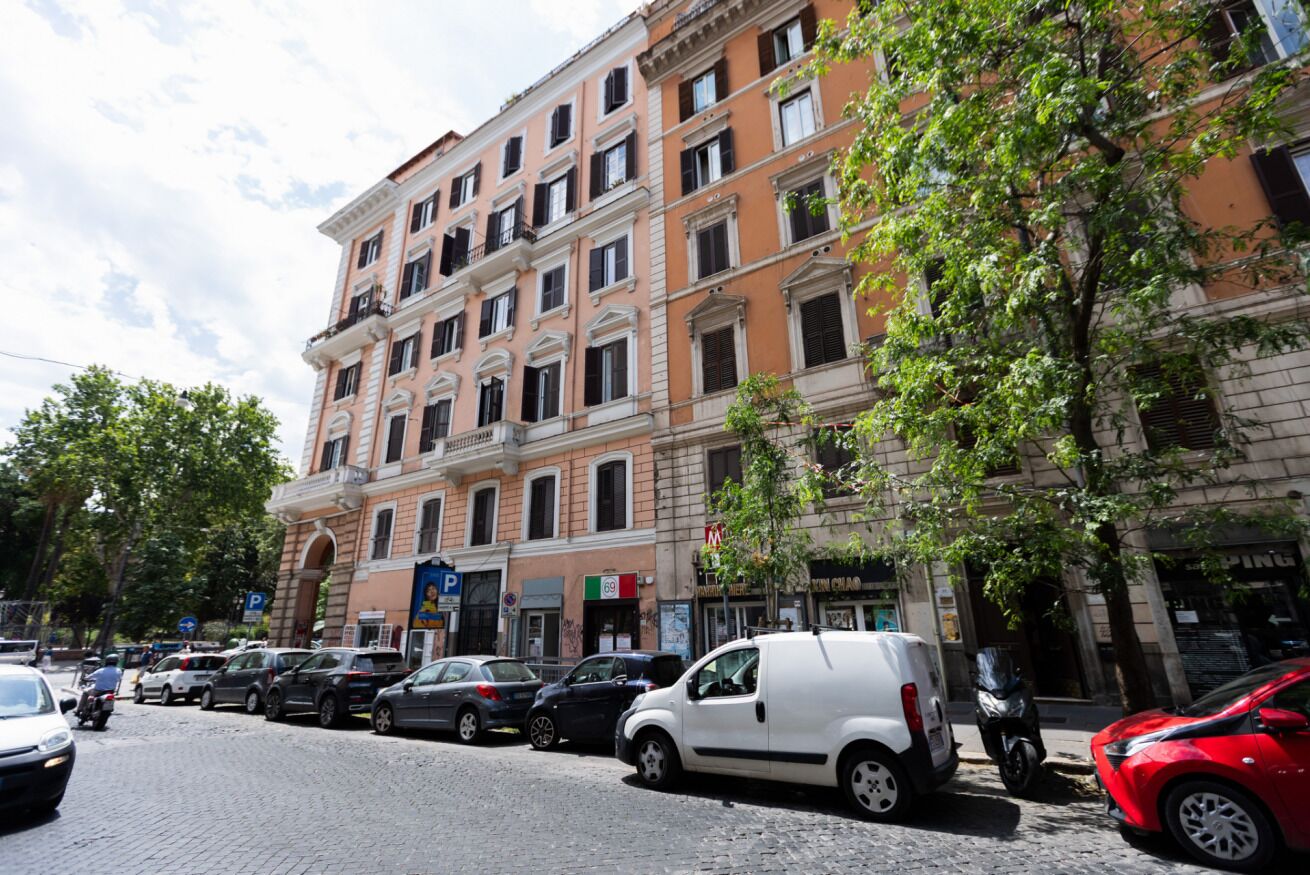 A multi-story building with a row of parked cars on the street.