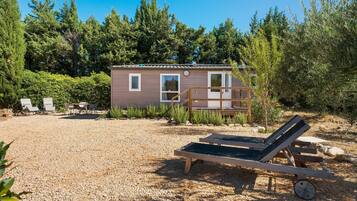 Une petite cabane dotée d’une terrasse, entourée de gravier et de verdure.