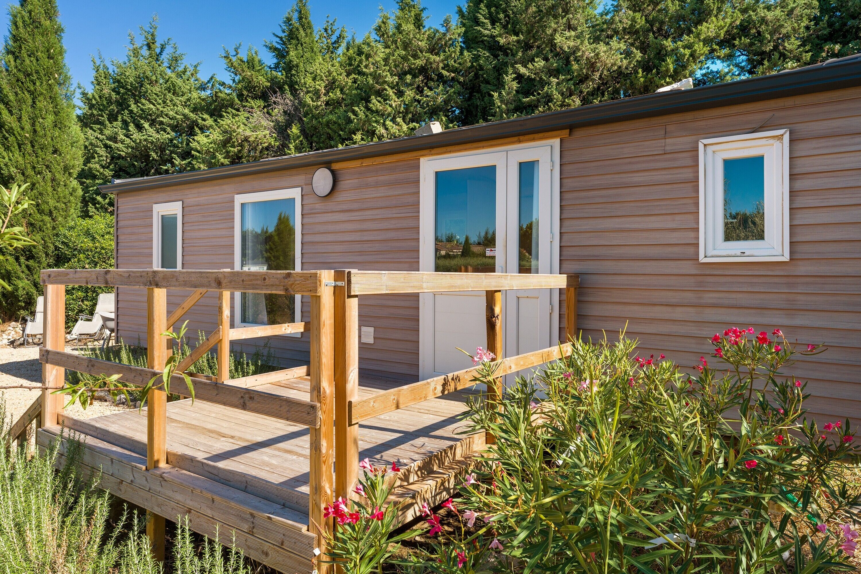 A wooden cabin with a deck, large windows, and a view of trees.