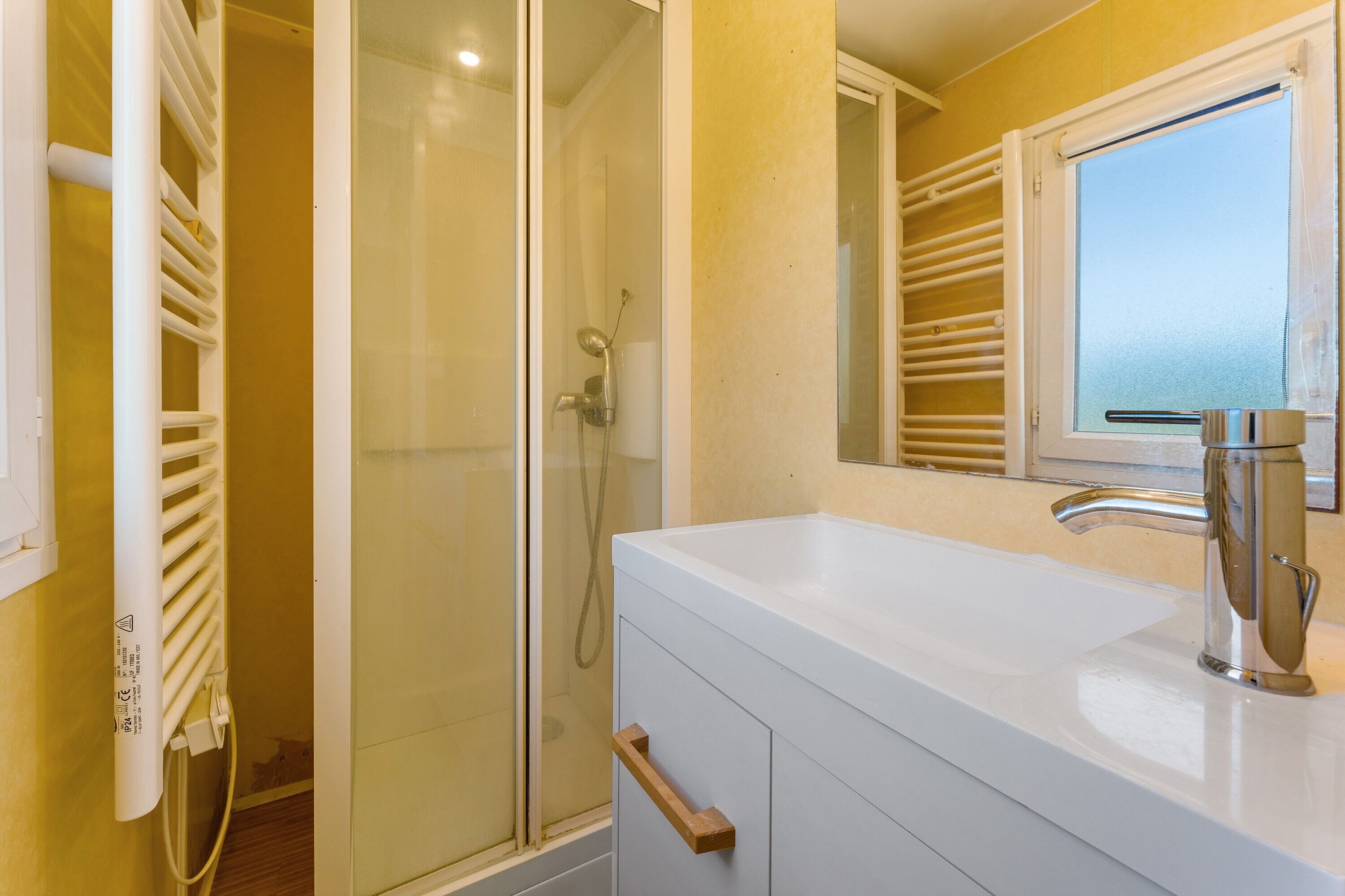 Une salle de bain avec une douche à parois de verre, un lavabo blanc avec un robinet chromé et un miroir au-dessus du lavabo.