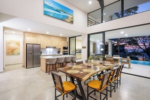 Une cuisine moderne dotée d’un îlot central, d’un coin repas avec une grande table et des chaises, et offrant une vue sur une piscine.