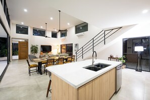 A modern kitchen with a central island, dining area, and a staircase leading to an upper level. - New Listing • Casa Azul Oasis • Pacifico 4BR Villa • Private Pool (Playas del Coco)