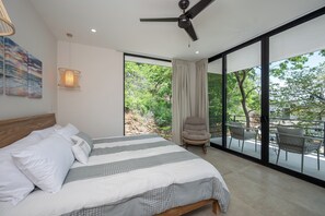 A bedroom with a bed, a ceiling fan, a large window with curtains, and a balcony with chairs. - New Listing • Casa Azul Oasis • Pacifico 4BR Villa • Private Pool (Playas del Coco)