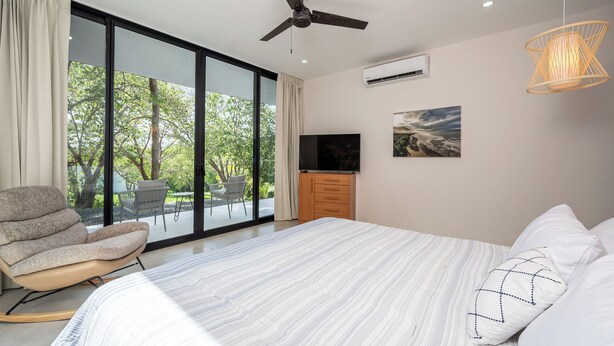 Una camera da letto moderna con un letto grande, un ventilatore a soffitto, una TV e vista sul verde.