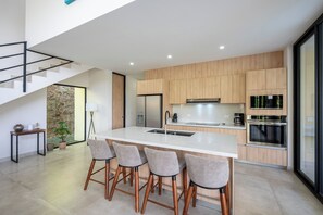 A modern kitchen with a central island, bar stools, and built-in appliances. - New Listing • Casa Azul Oasis • Pacifico 4BR Villa • Private Pool (Playas del Coco)