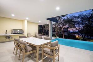 Un espace extérieur moderne aménagé pour les repas, avec une piscine, un barbecue et une vue sur les arbres.