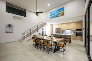 A modern kitchen with wooden cabinets, a built-in oven, and a dining area with a wooden table and chairs. - New Listing • Casa Azul Oasis • Pacifico 4BR Villa • Private Pool (Playas del Coco)