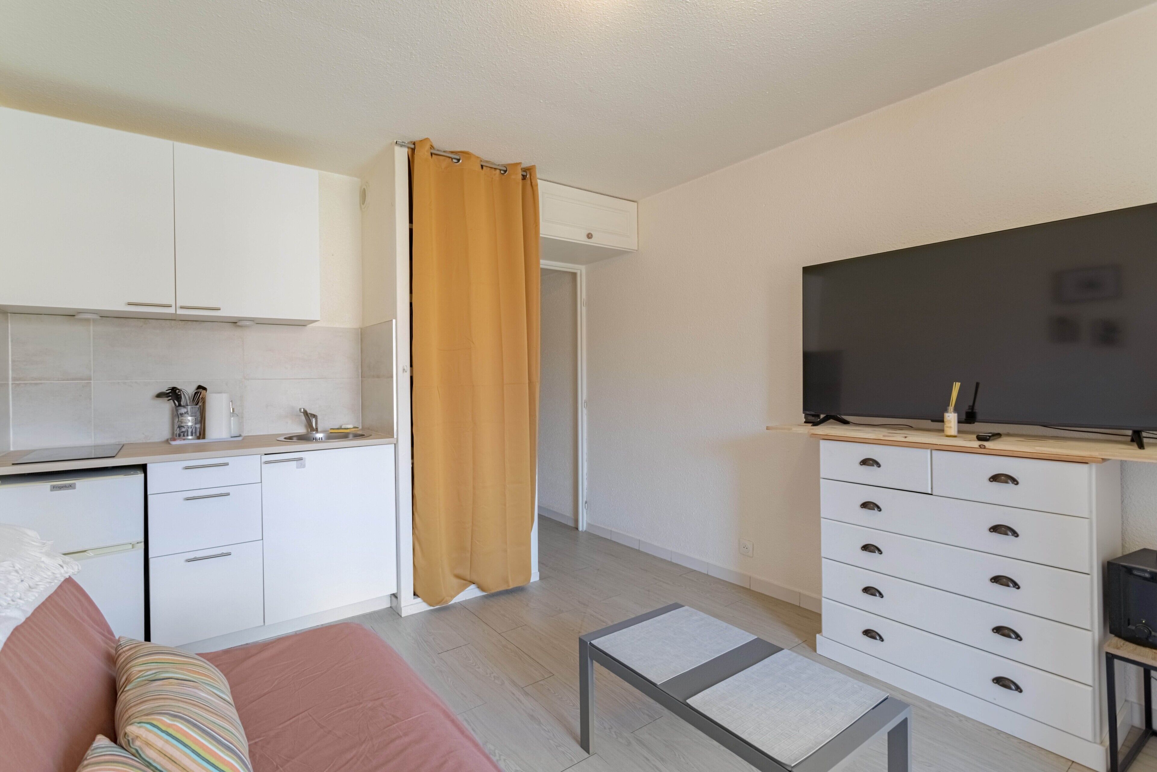 Ein gemütlicher, kompakter Wohnraum mit Küchenzeile, einer Couch, einem Fernseher und einem kleinen Tisch.