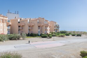 Ein mehrstöckiges Wohngebäude mit Balkonen, einem gepflasterten Innenhof und Blick auf den Strand.