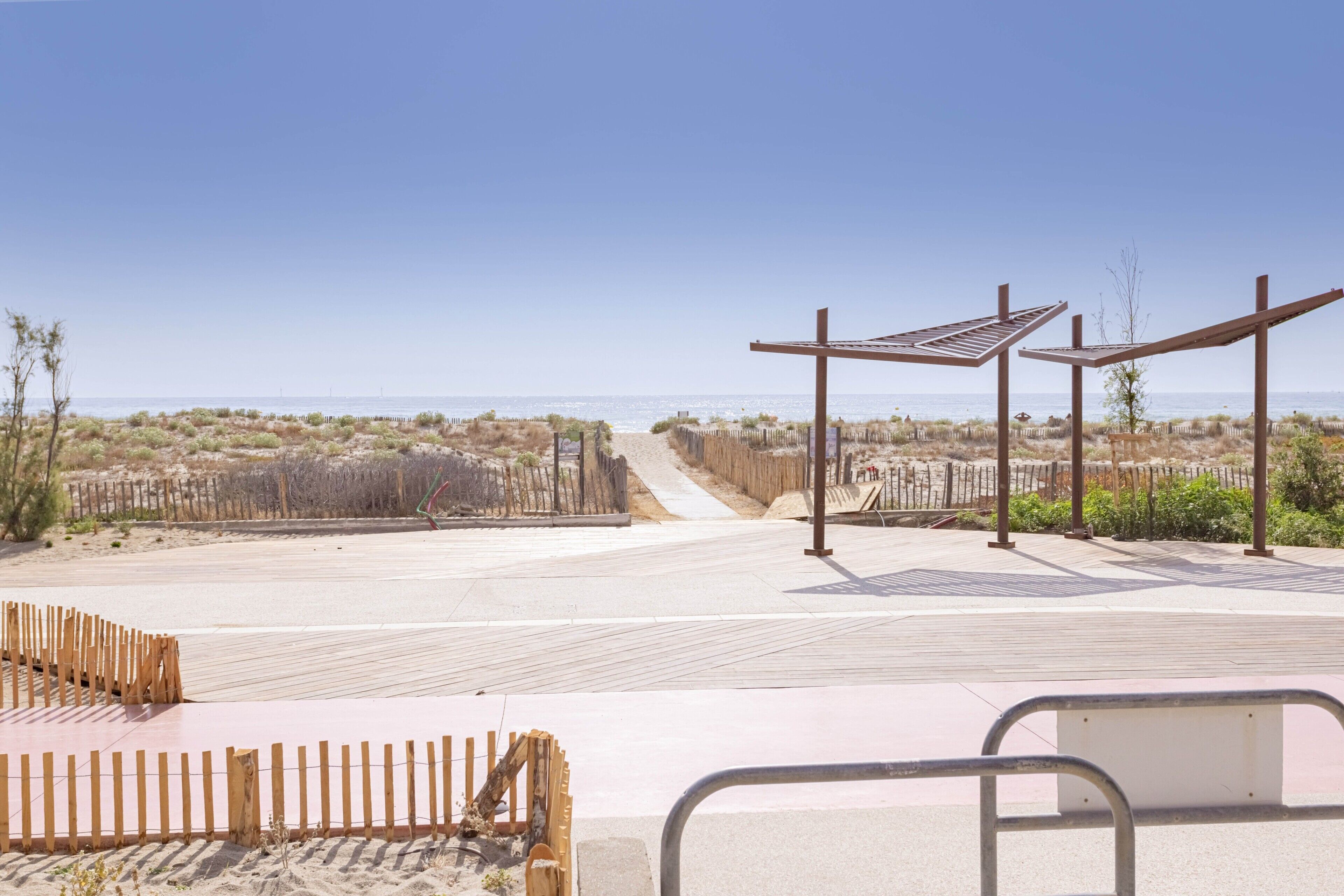 Eine Strandpromenade mit Holzzäunen, einem Sandweg und Blick aufs Meer.