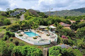 A resort with a swimming pool, lounge chairs, and a view of the surrounding hills. - New Listing • 2BR Ocean View Condo • Coco Joya • Walk to the Beach (Playas del Coco)