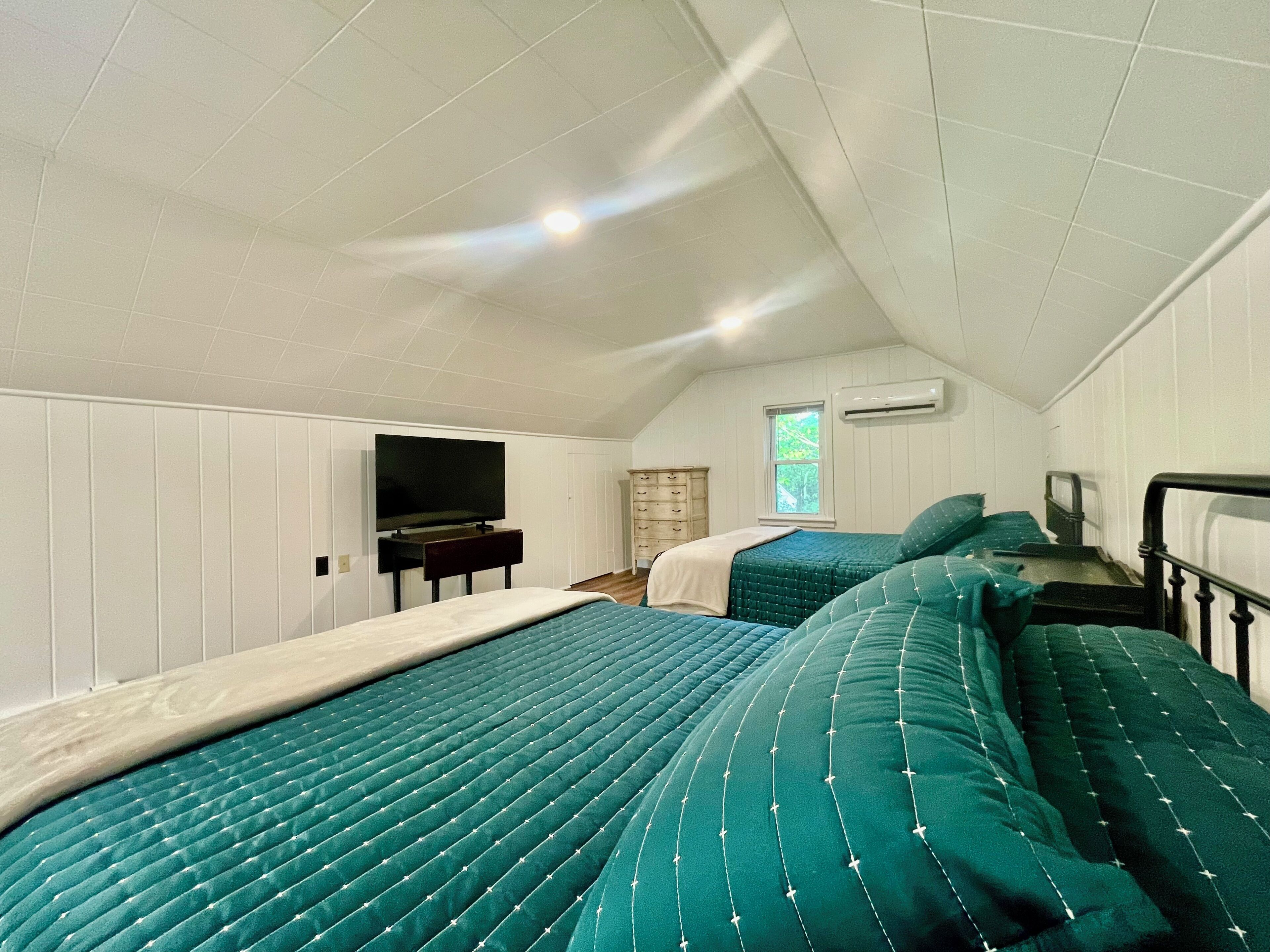 Une chambre avec deux lits, une télévision, une commode et un appareil de climatisation.