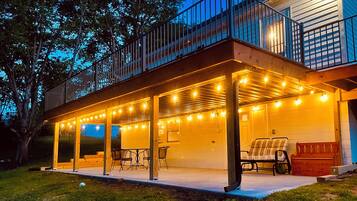 Une terrasse extérieure couverte, agrémentée de guirlandes lumineuses, d’un banc et d’une table.