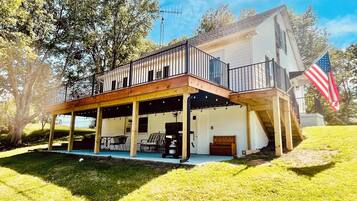 Une maison à deux étages avec un patio couvert, un drapeau américain et un grand arbre en arrière-plan.
