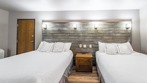 A hotel room with two beds, a wooden headboard, bedside lamps, and a nightstand with a clock.