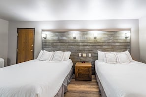 A hotel room with two beds, a wooden headboard, bedside lamps, and a nightstand with a clock.
