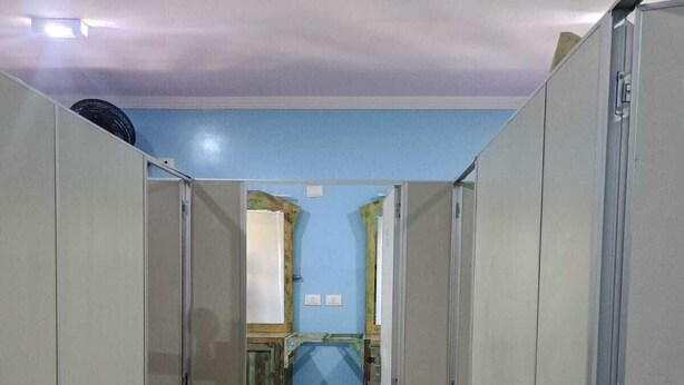 Un pasillo con taquillas a ambos lados, que conduce a una habitación con pared azul y ventana.