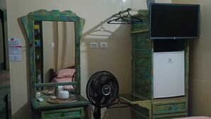 Una habitación de hotel con una cama, un aparador, un espejo, un ventilador, una televisión y un refrigerador pequeño.